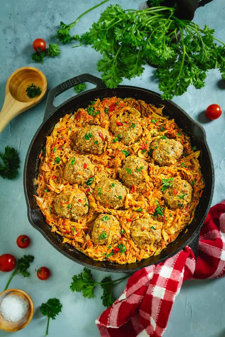 Cast-iron skillet with unstuffed cabbage rolls on a blue background.