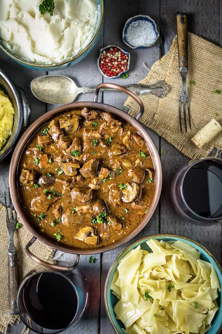 a flat lay of Instant pot beef stew on a gray wood table with bowls of pasta and potato mash