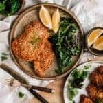 A plate with breaded meat, greens and lemons on a rustic table