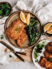 A plate with breaded meat, greens and lemons on a rustic table