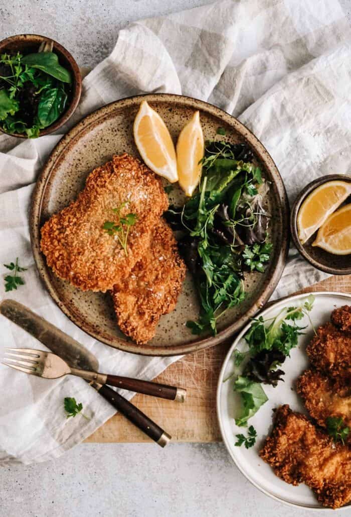 A plate with breaded meat, greens and lemons on a rustic table