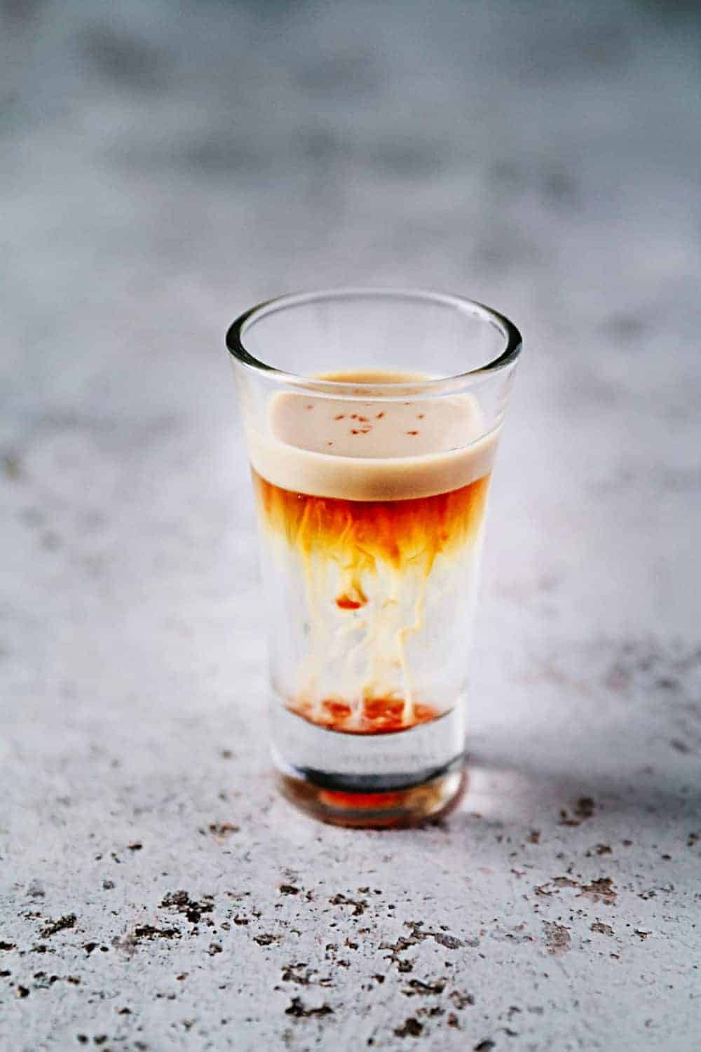 A small shot glass with jellyfish beverage sitting on a gray counter