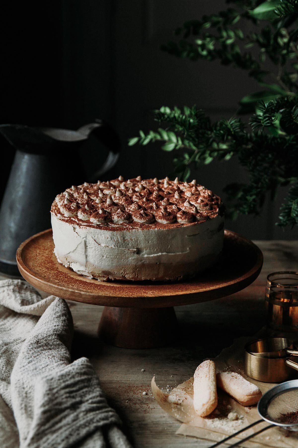 Tiramisu cheesecake on a cake stand with kitchen towel on a rustic table