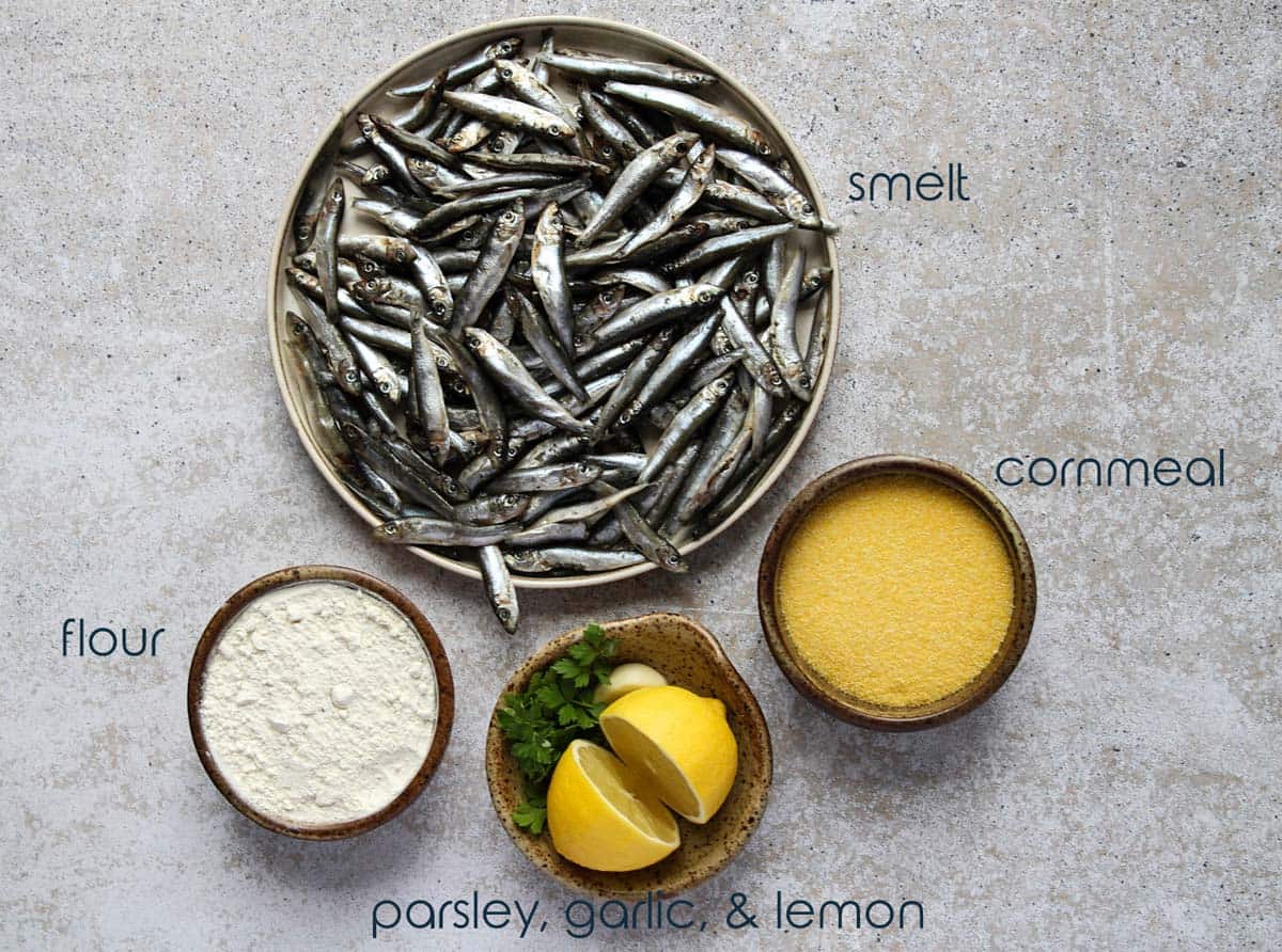 A plate with fresh smelt and small bowls with flour, cornmeal, and lemons