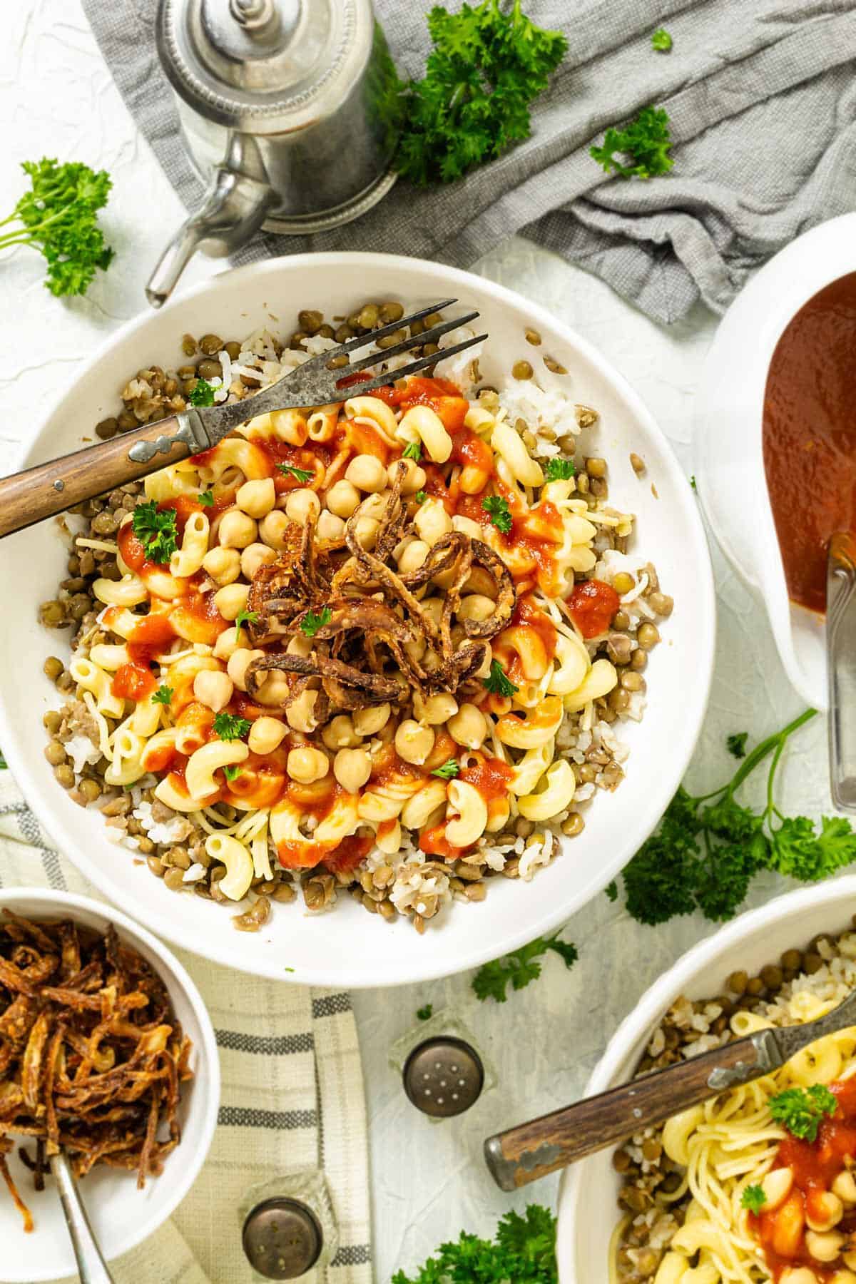 Kushari dish in a bowl sitting on the table with other condiments and food.