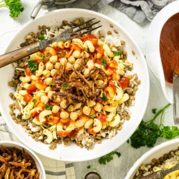 Kushari dish in a bowl sitting on the table with other condiments and food.