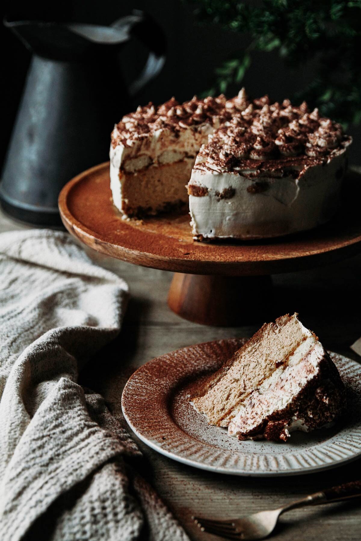 A cake on a wooden cake stand with a slice sitting on a plate