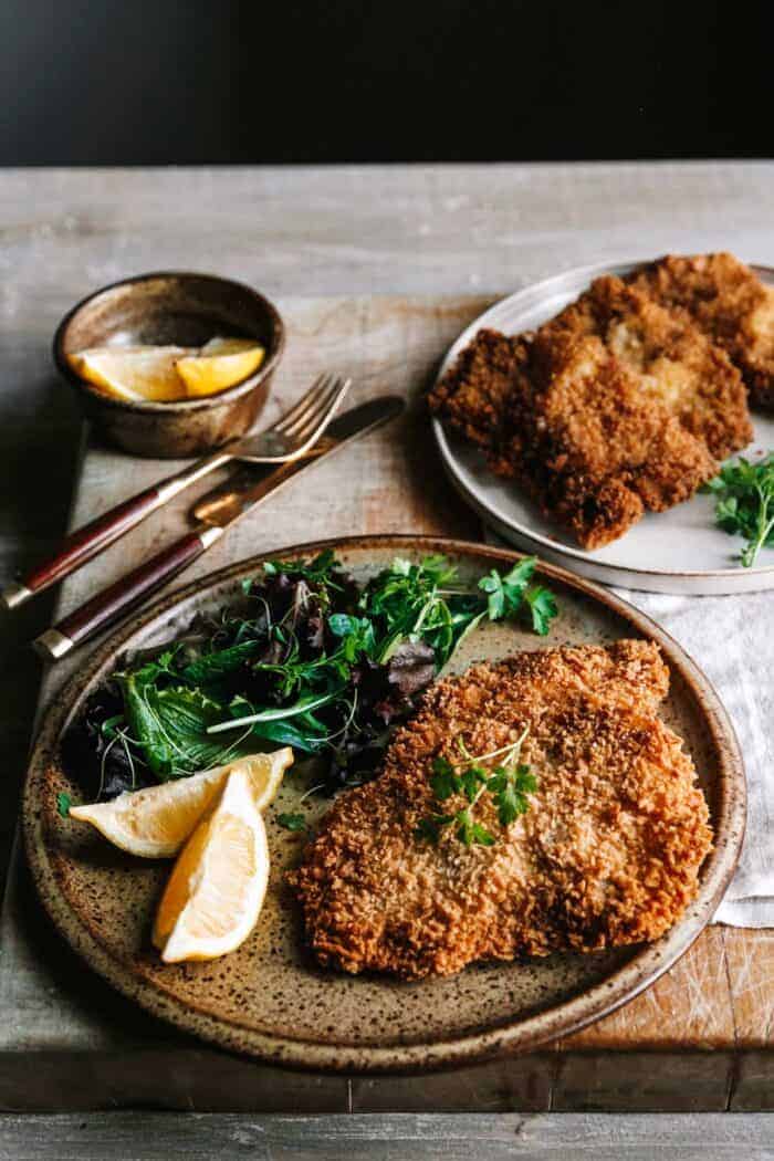 Food on a plate sitting on a wooden table with schnitzel