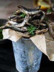 A close up of fried smelt fish in a small bucket.