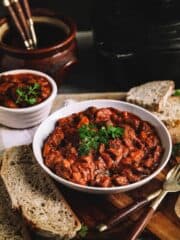 A lage and a small plaate of beef stew on a wooden table with bread and utensils