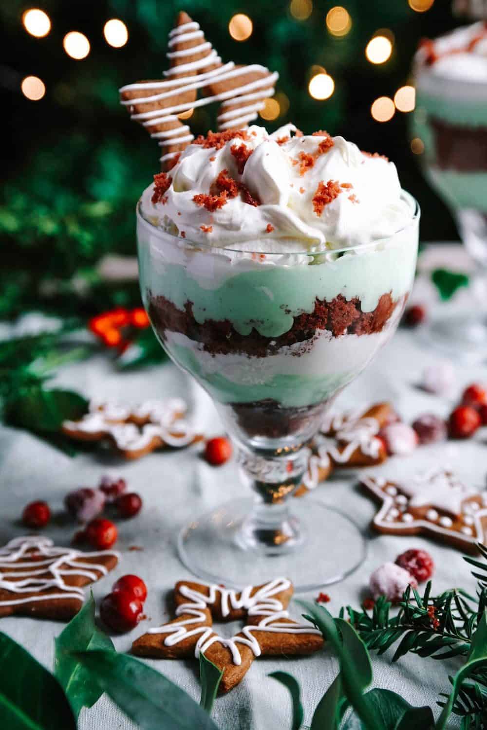 A closeup of the triffle in a glass with Christmas decorations and lights in the background.