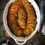 An oval dish with slices of crispy roasted sweet potatoes sitting on a table.