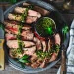 Slices of grilled steak ion a platetopped with chimichurri parsley sauce