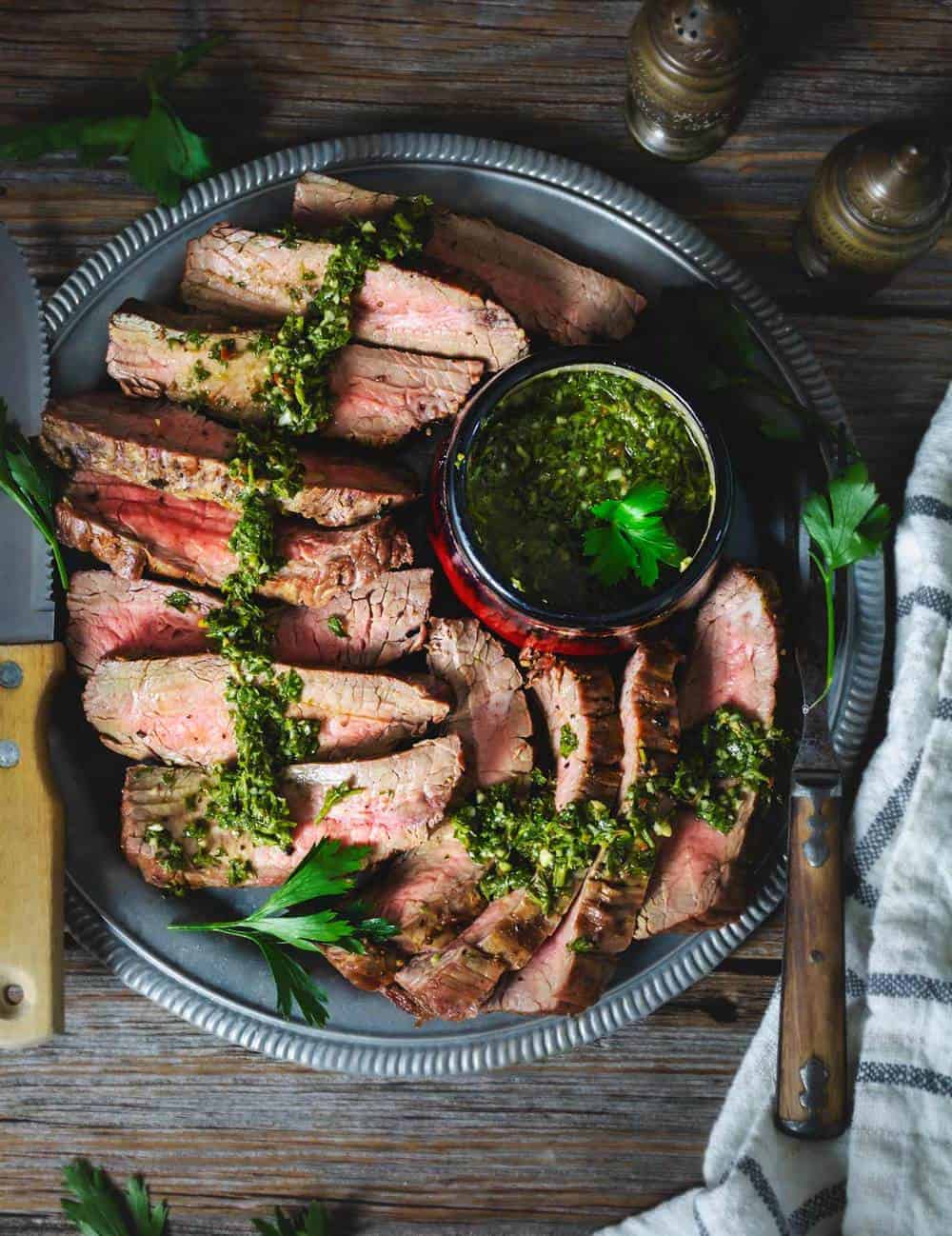 Slices of grilled steak ion a platetopped with chimichurri parsley sauce