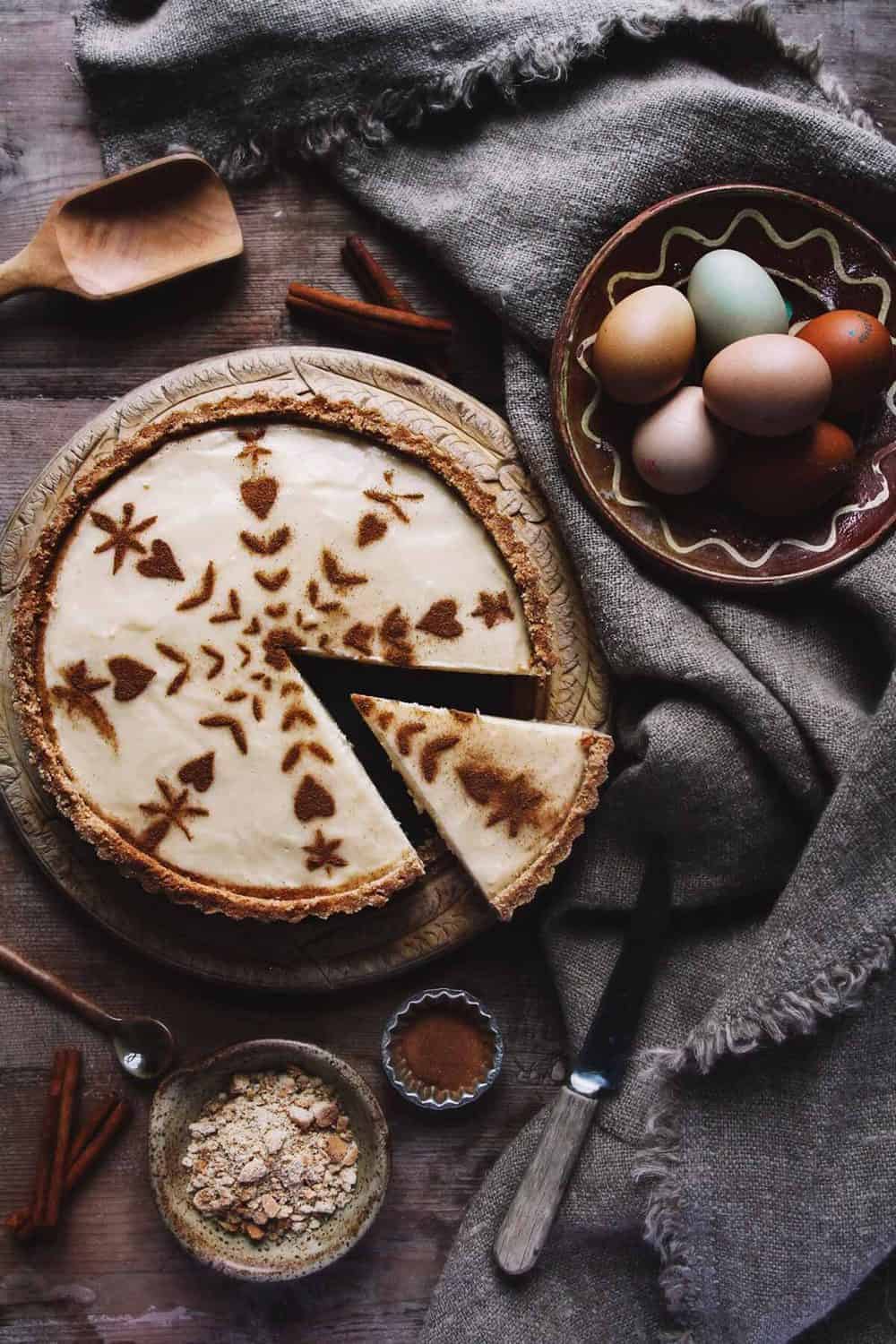 A rustic milk tart on a table with eggs, tablecloth, and cinnamon.