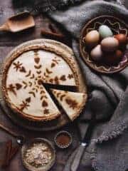 A rustic milk tart on a table with eggs, tablecloth, and cinnamon.
