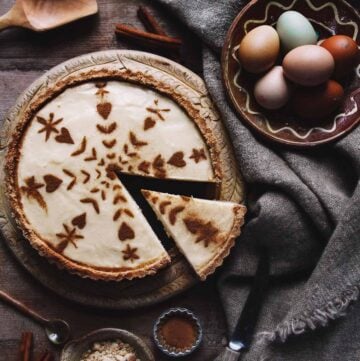 A rustic milk tart on a table with eggs, tablecloth, and cinnamon.