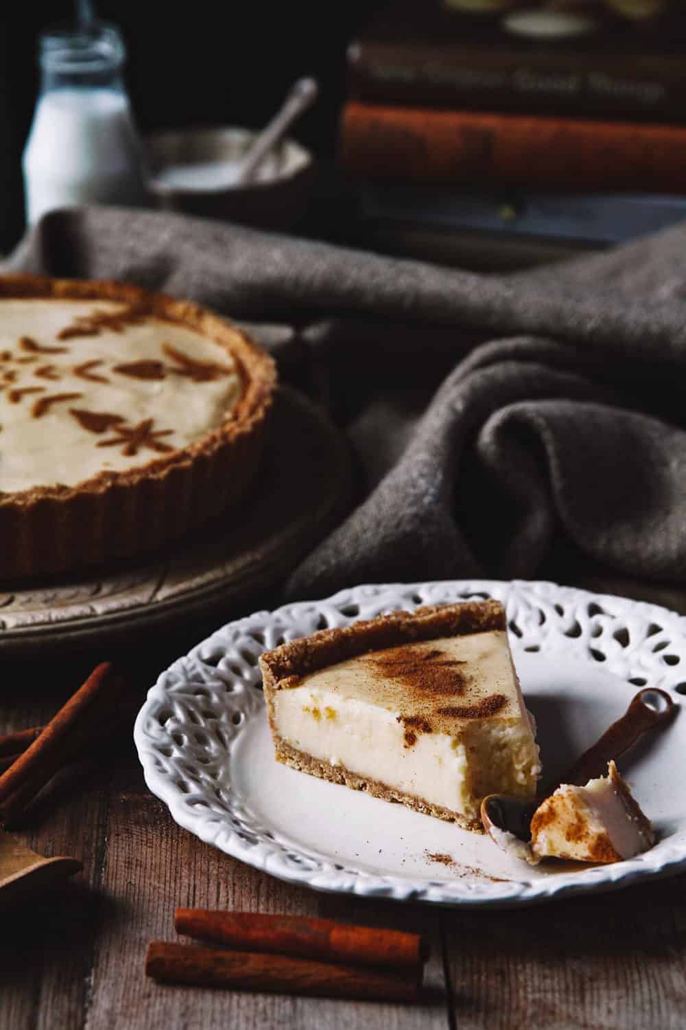 A slice of creamy milk tart on a white plate sitting on a rustic table.