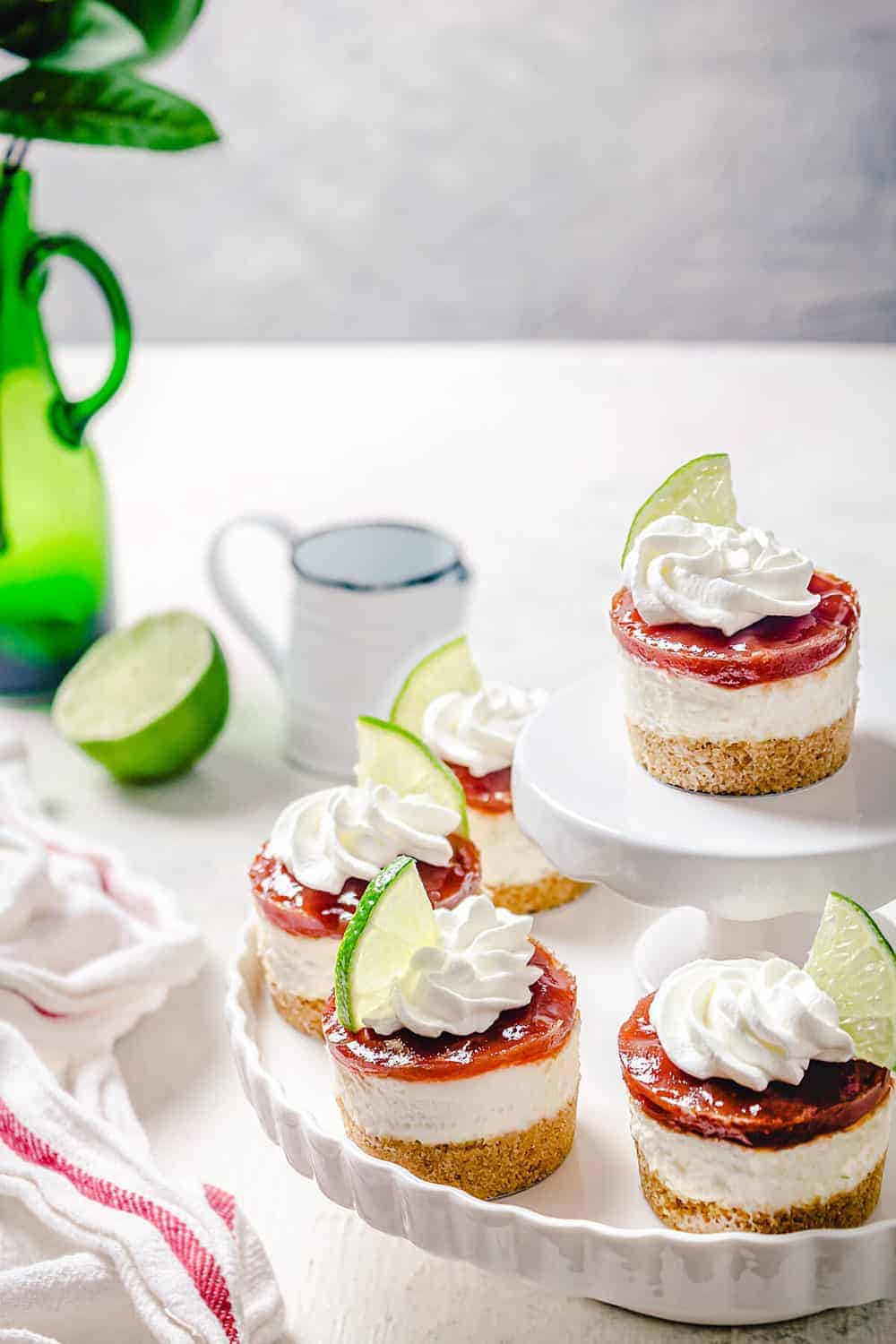 Individual cheesecakes on a white plate served on a white table with lime slices.