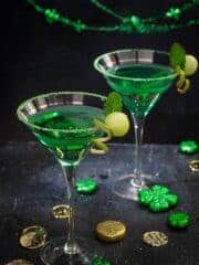 Two martini glasses with green cocktail on a black background.