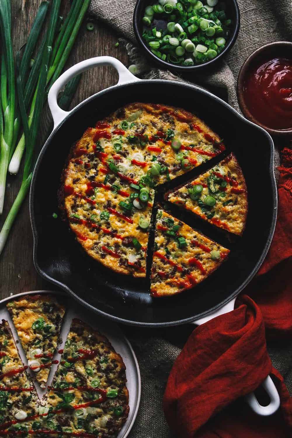 Omelet in a skillet sliced into wedges and topped with green onions.