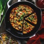 Omelet in a skillet sliced into wedges and topped with green onions.