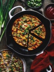 Omelet in a skillet sliced into wedges and topped with green onions.