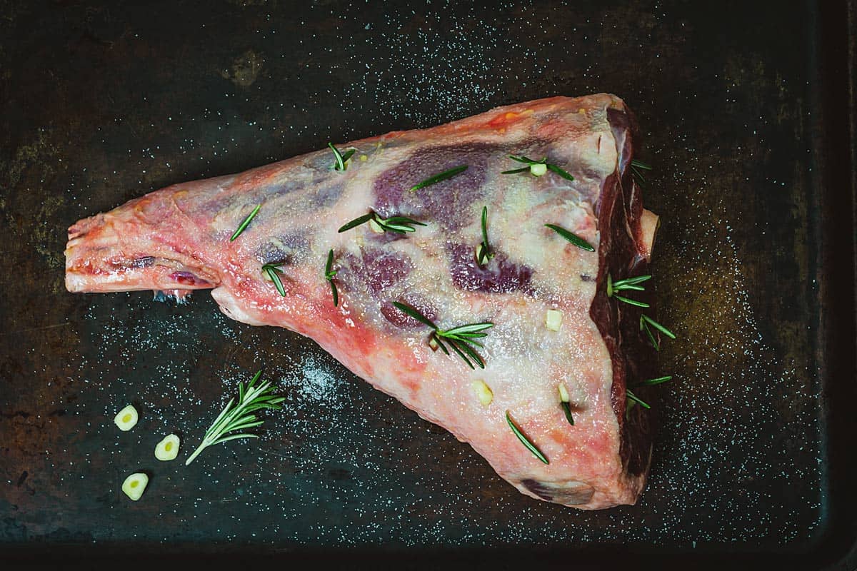 A leg of lamb spiked with garlic and rosemary, ready for the oven.