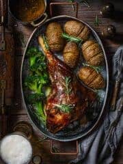 Finished recipe of lamb meat with beer on a metal roasting pan with potatoes and broccoli on a wooden table.