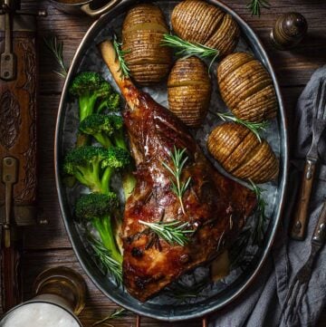 Finished recipe of lamb meat with beer on a metal roasting pan with potatoes and broccoli on a wooden table.