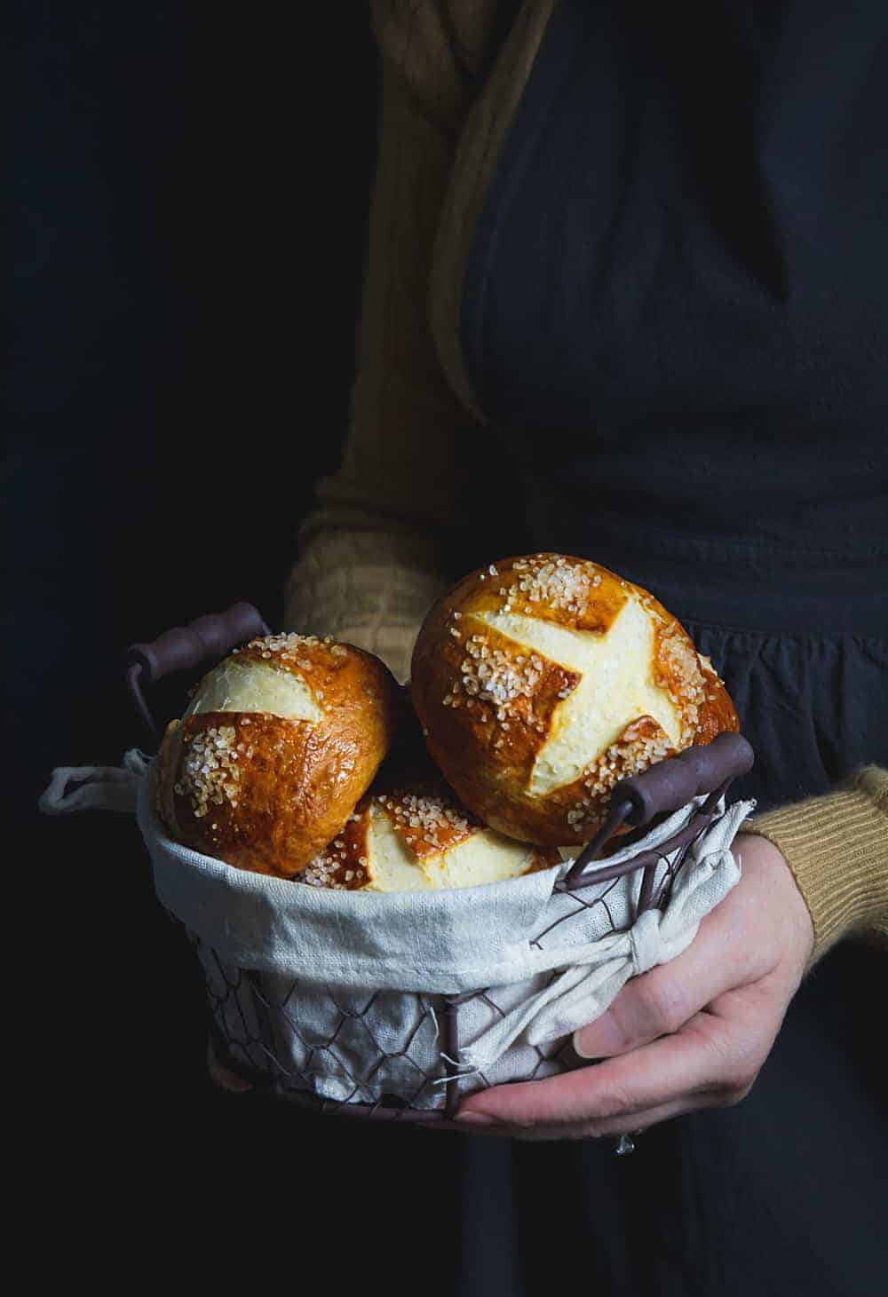 A woman holding a basket with pretzel rolls.