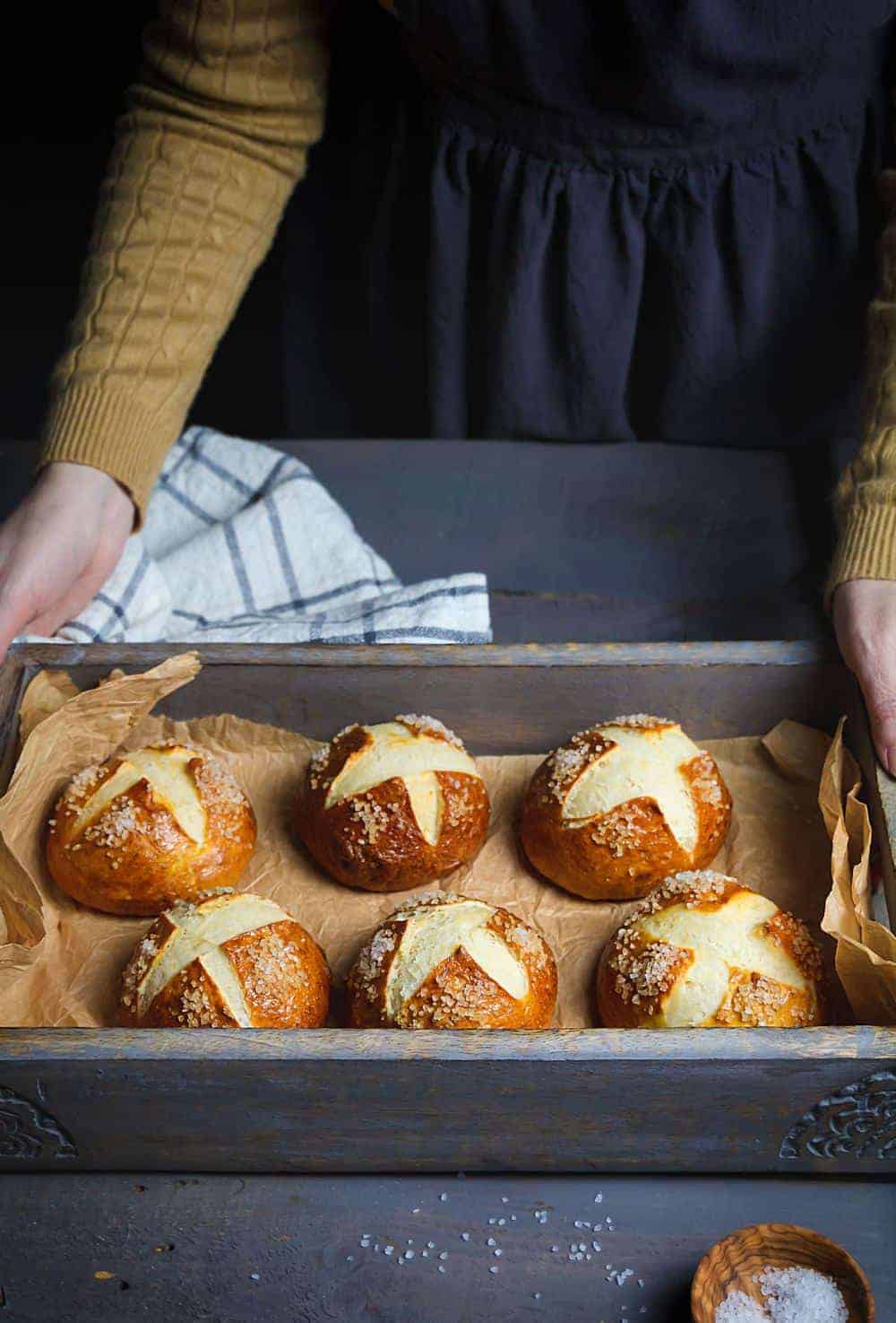 A person setting down a wooden tray lined with pretzel buns.