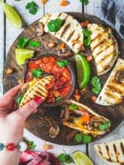 A woman dipping steak quesadilla into a bowl with salsa with more quesadillas spread on a wooden plank.