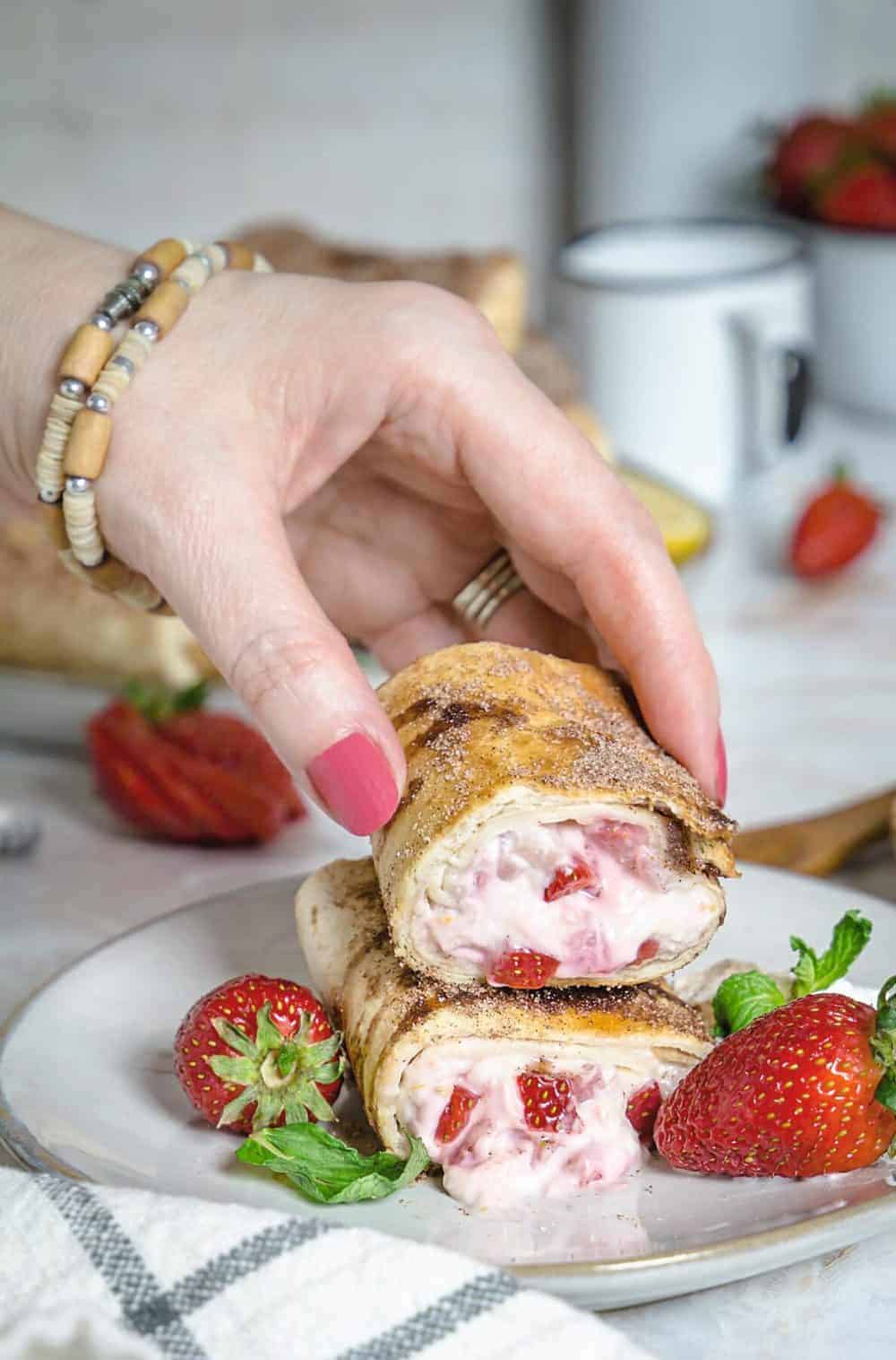 A hand grabbing one half of strawberry cheesecake chimichanga.