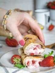 A hand grabbing one half of strawberry cheesecake chimichanga.