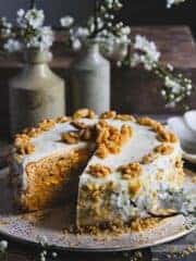 Carrot cake cheesecake on a cake stand with one slice removed.