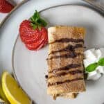 Chimichanga on a plate with chocolate drizzle, lemon, whipped cream, and strawberry.