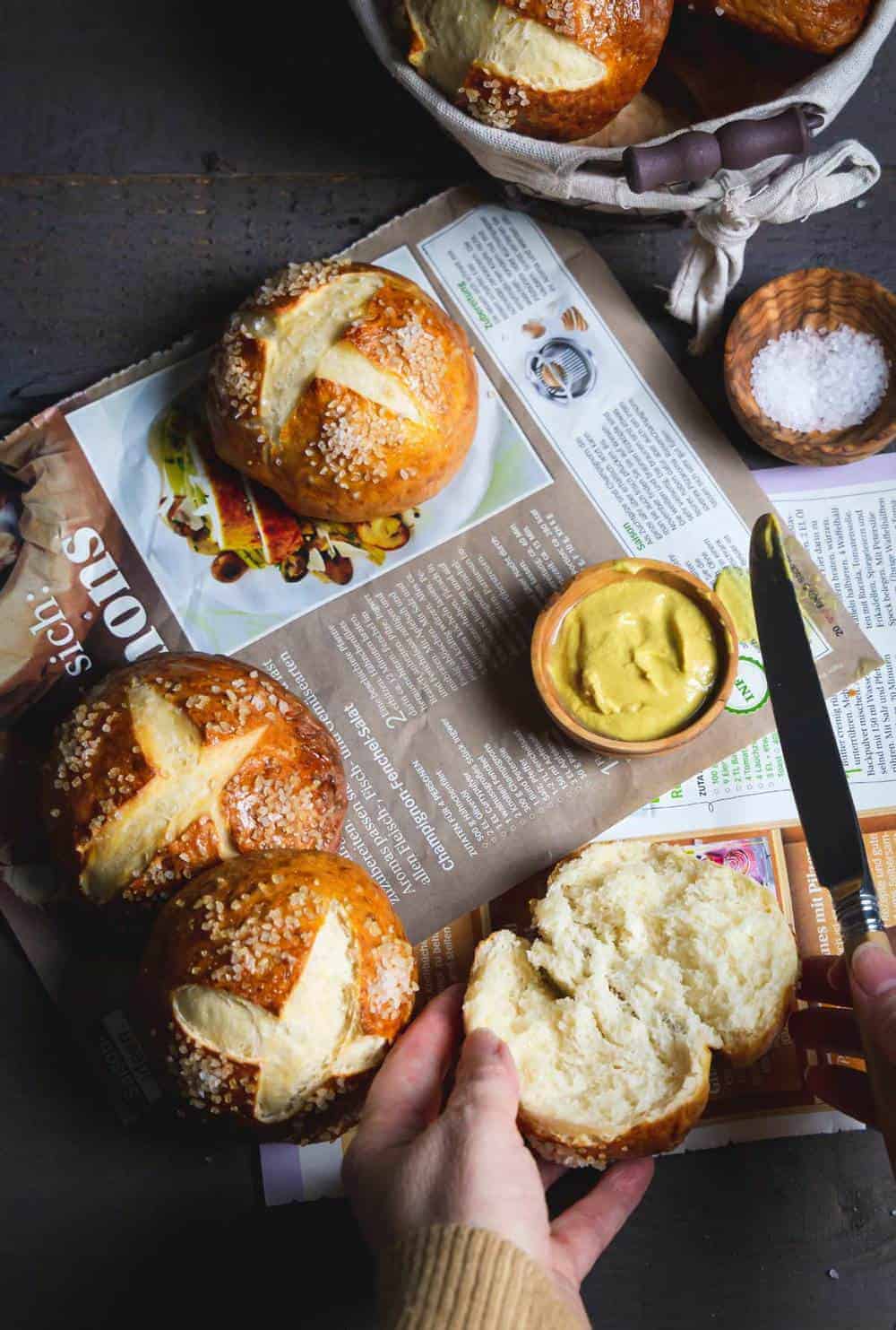 A person splitting the pretzel bun over a magazine in German with more rolls on top of it.