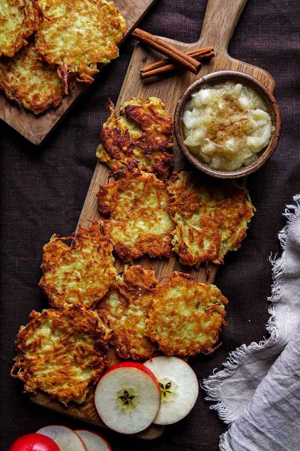 Potato pancakes on a wooden board in a single layer with applesauce.