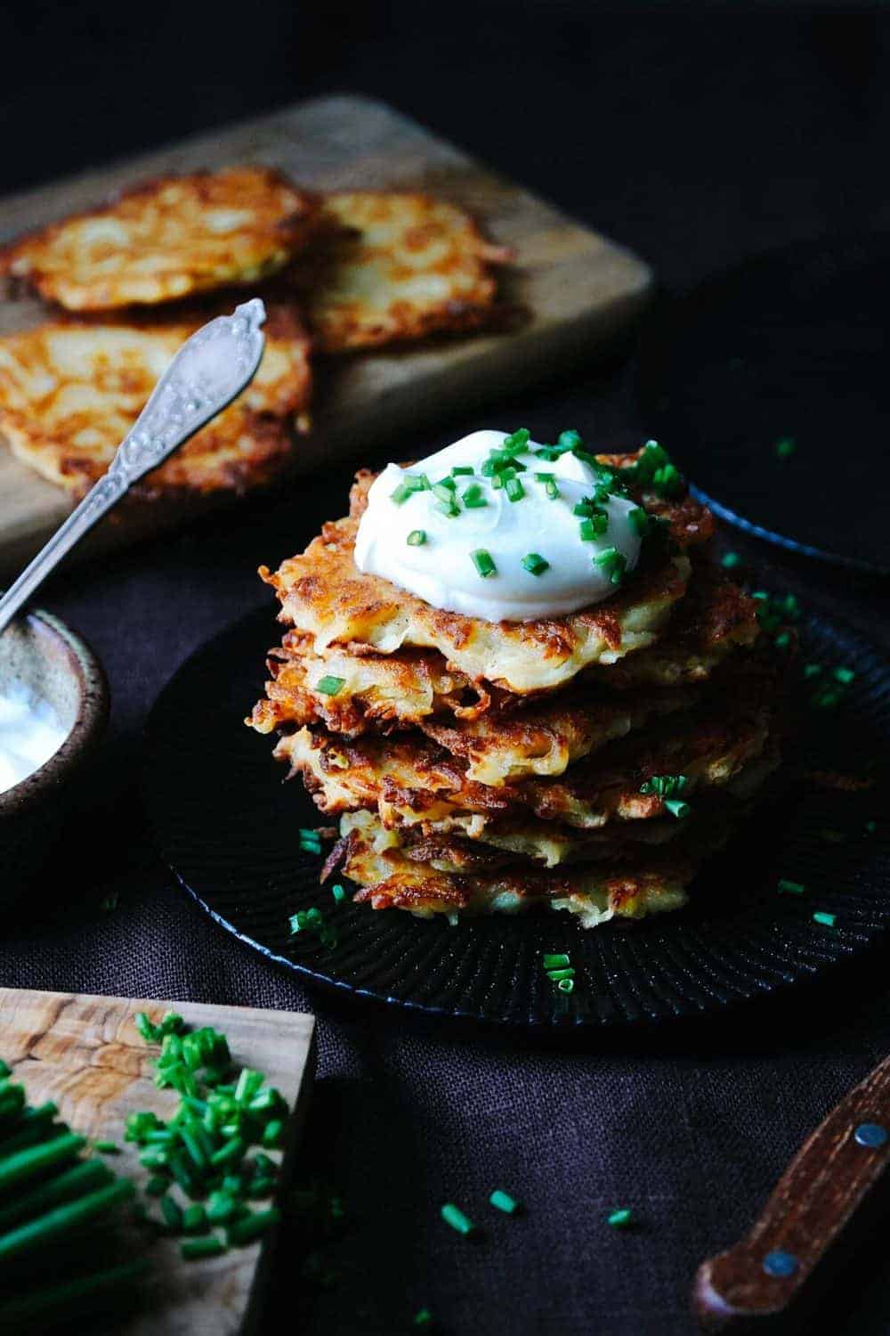 A stack of Kartoffelpuffer on a black plate, topped with sour cream and chives.