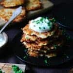 A stack of Kartoffelpuffer on a black plate, topped with sour cream and chives.