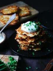 A stack of Kartoffelpuffer on a black plate, topped with sour cream and chives.