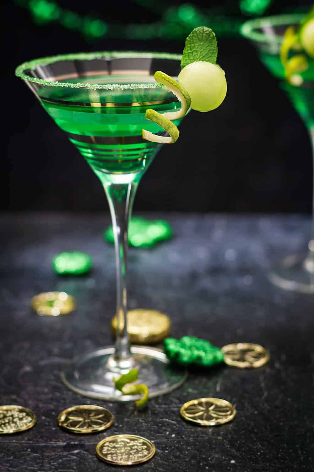 One martini glass with green martini on a black table with Irish decorations.