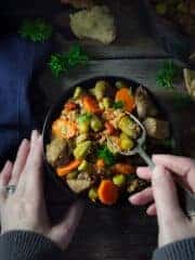 A bowl of okra and meat stew on a wooden table with woman's hands holding the bowl and a spoon.