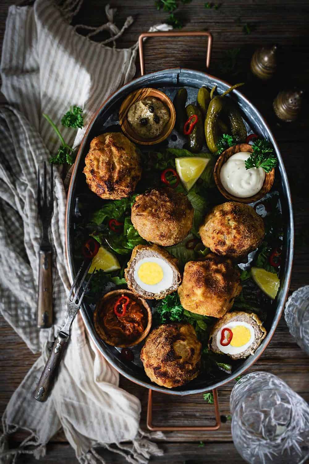 An oval tray with air fried Scotch eggs on a bed of lettuce with dipping sauces.