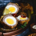 Scotch egg halves in an oval tray with lemon wedges and hot pepper rings.