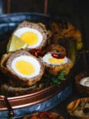 Scotch egg halves in an oval tray with lemon wedges and hot pepper rings.