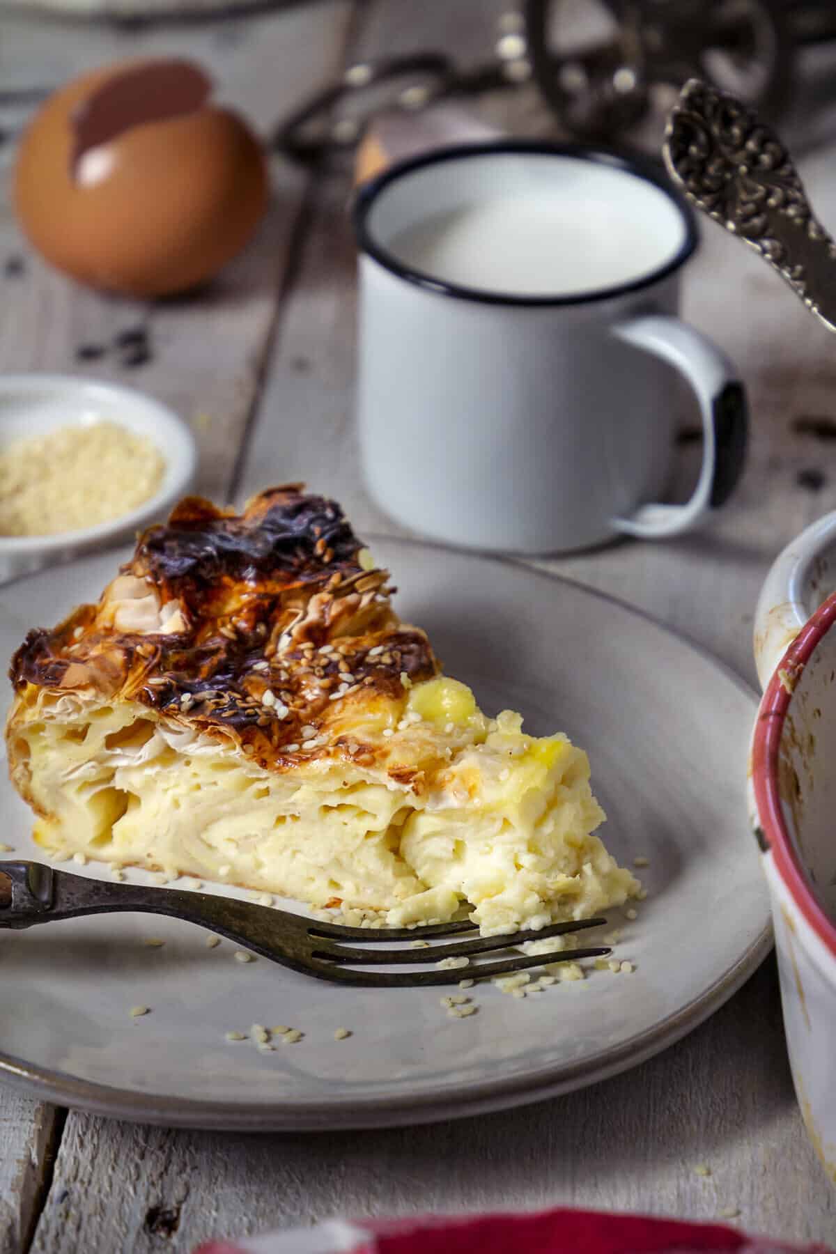 A close up of the slice of savory egg pie on a plate and cup of milk in the background.