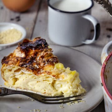 A close up of the slice of savory egg pie on a plate and cup of milk in the background.