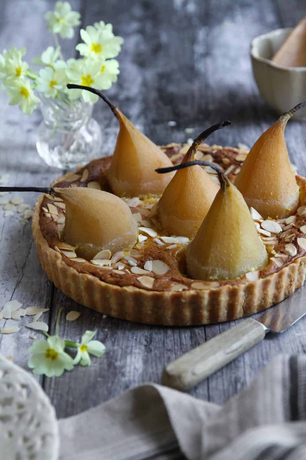 A French almond tart with whole poached pears sitting on a gray background.